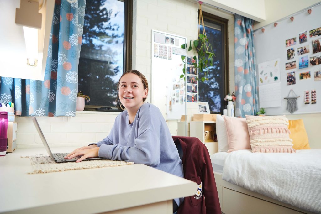 A happy girl is seated at a desk in her dorm room at 鶹ƵAV Anglican Girls School.