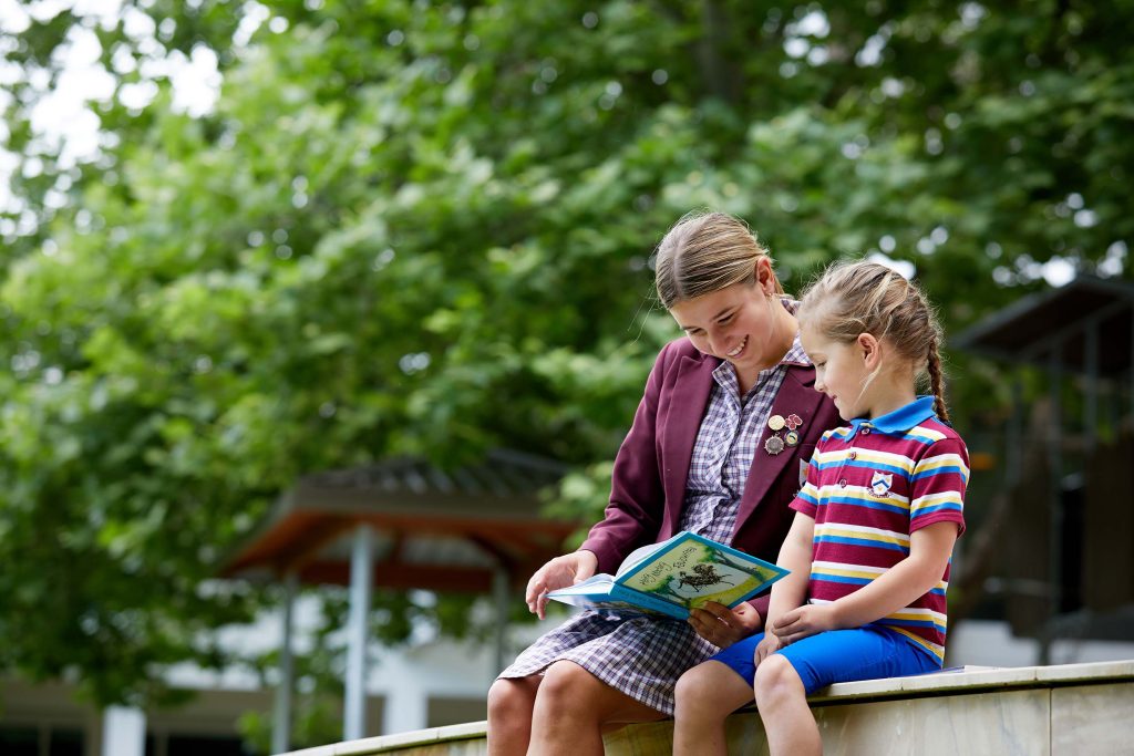 A teenager and child reading book on bench at 鶹ƵAV Anglican Girls School.