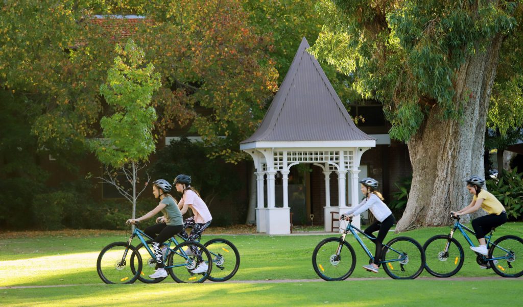 Four people riding bikes in a park at 鶹ƵAV Anglican Girls School, surrounded by 16 hectares of green grounds in Karrinyup and Trigg Bushland Reserve. Boarding School In Perth. 