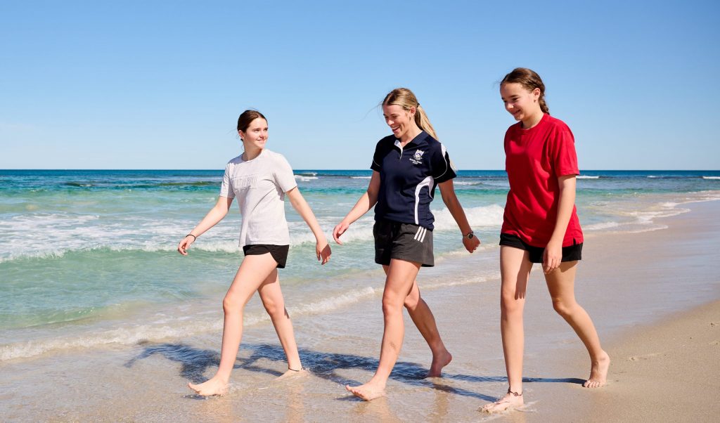 Three young women from 鶹ƵAV Anglican Girls School walking on the beach, holding hands. Boarding School In Perth. 