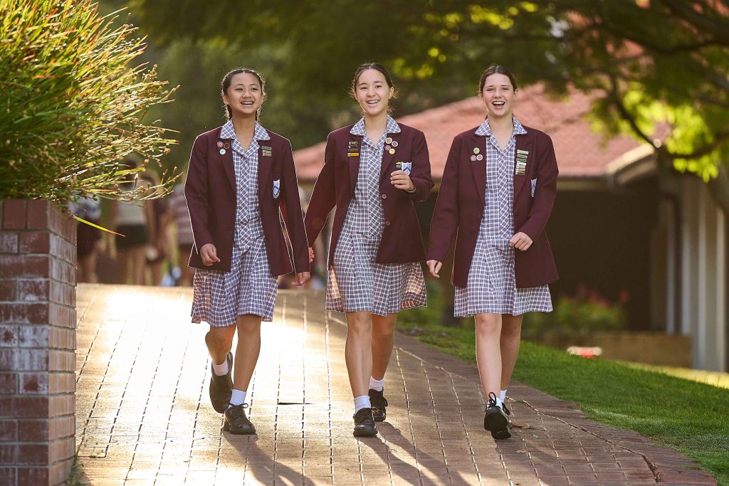 Three girls in school uniforms walking down a brick path at 鶹ƵAV Anglican Girls School.