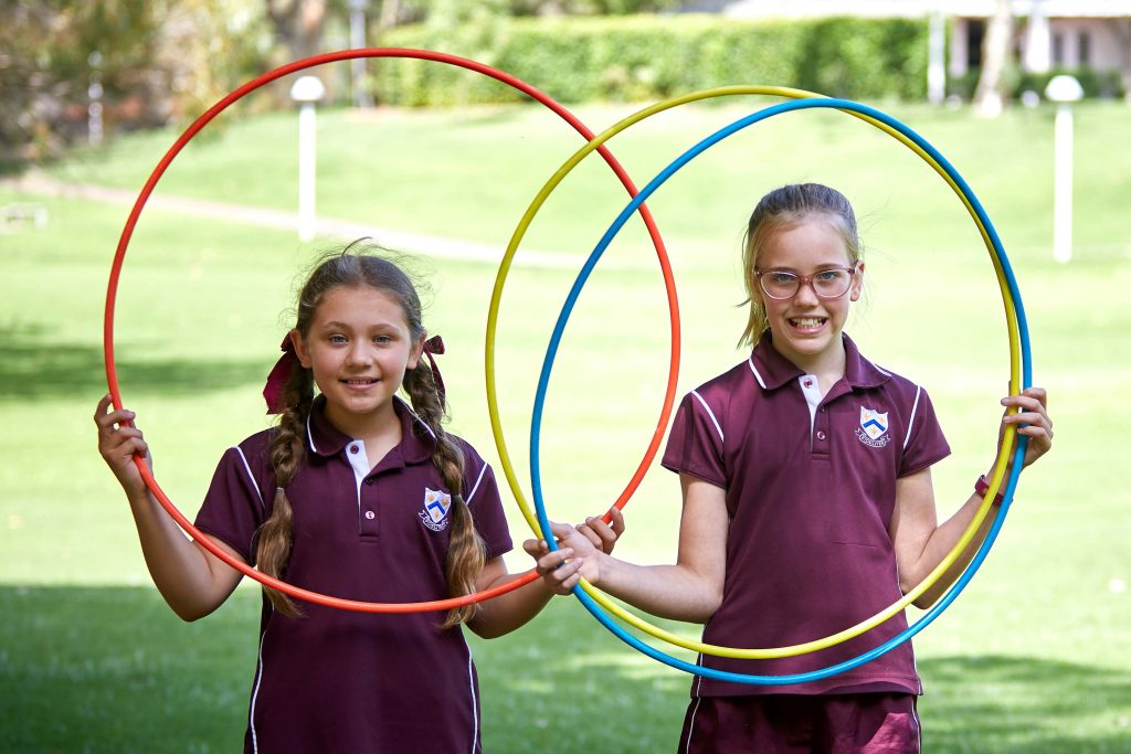 Two girls from 鶹ƵAV Girl's boarding School hold hula hoops in the grass.
